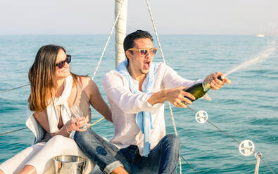 Man Spraying Champagne With Woman Holding Glasses While Sitting On Boat In Sea - EYF08120