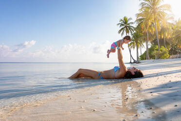 Seitenansicht der Mutter, die mit ihrer Tochter spielt, während sie am Ufer des Strandes liegt - EYF08204