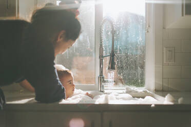 Mutter badet Sohn in der Küchenspüle am Fenster zu Hause - EYF08208