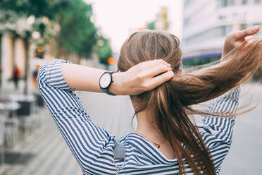 Rückansicht einer Frau, die sich die Haare bindet, während sie auf der Straße in der Stadt steht - EYF08219