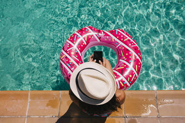 Directly Above Shot Of Woman With Inflatable Holding Smart Phone In Swimming Pool - EYF08231