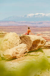 Wanderin im Sport-BH ruht sich auf einem großen Felsen mit Blick auf die Canyonlands aus - CAVF85829