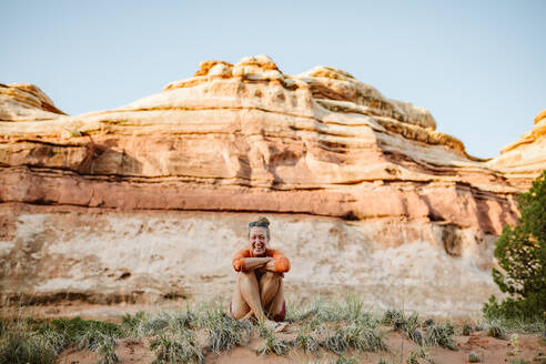 Blonde Frau sitzt im Schneidersitz und lacht in der Wüste von Utah - CAVF85853