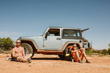 Portrait of two straight faced hikers sitting in front of jeep - CAVF85855
