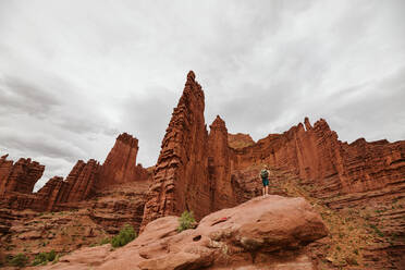 Male hiker looks up at the fisher towers near moab utah - CAVF85865