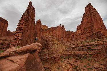 Fischertürme aus rotem Sandstein erheben sich über einen männlichen Wanderer in der Nähe von Moab, Utah - CAVF85866