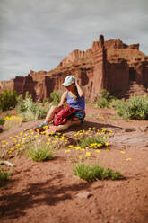 Wanderin rückt ihren Hut zurecht, während sie sich zwischen gelben Wüstenblumen ausruht - CAVF85874
