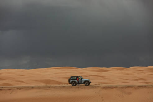 Frau und ihr Jeep bei der Fahrt über Sanddünen unter stürmischem Himmel - CAVF85911