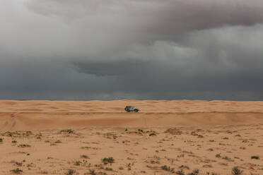 Einsames Auto unter stürmischen Regenwolken während eines Mikroausbruchs in der Wüste - CAVF85914