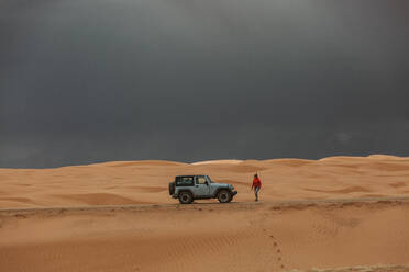 Frau geht zurück zum Jeep unter stürmischem Himmel in den Sanddünen von Utah - CAVF85916