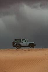 Jeep fährt über eine Sanddüne auf einer unbefestigten Straße unter Gewitterwolken - CAVF85918