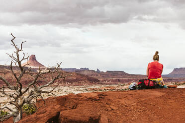 Weibliche Rucksacktouristin sitzt auf ihrem Rucksack, während sie eine Pause in der Wüste von Utah macht - CAVF85953