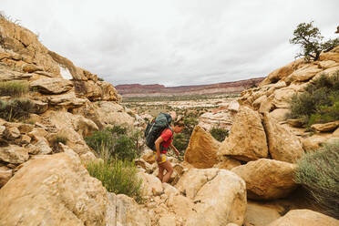Female backpacker hikes over rocky rugged terrain in utah desert - CAVF85955