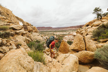 Weiblicher Rucksacktourist wandert über felsiges, zerklüftetes Terrain in der Wüste von Utah - CAVF85955