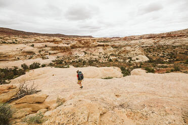 Female backpacker walks down a sandstone rock face in utah desert - CAVF85958
