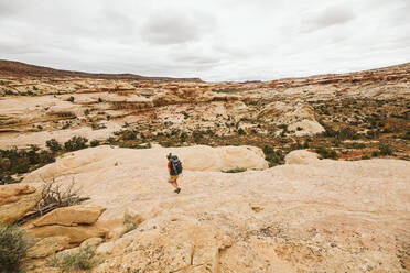 Weiblicher Rucksacktourist geht eine Sandsteinfelswand in der Wüste von Utah hinunter - CAVF85958