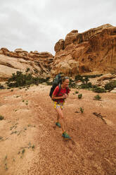 Lächelnde weibliche Backpacker Spaziergänge durch Canyon Boden in der Nähe von Moab Utah - CAVF85959