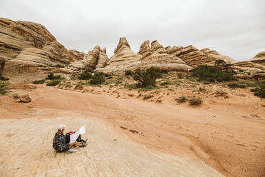 Wanderer schaut sich The Fins an und überprüft seine Karte auf einer Wanderung im Canyonland - CAVF85965