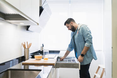 Man cooking in the kitchen in a denim shirt. A man is taking a cutlery - CAVF85981