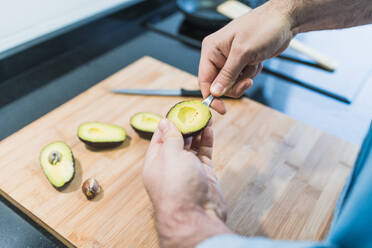 Man cooking in the kitchen in a denim shirt. An anonymous man is cooking avocados - CAVF85992