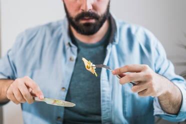 Auf dem Tisch steht ein Teller mit Pfannkuchen mit Käse und Avocado. Ein anonymer Mann isst gerade - CAVF85995