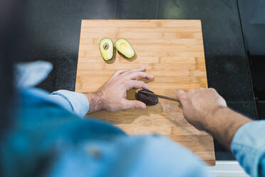 Man cooking in the kitchen in a denim shirt. An anonymous man is cutting avocados - CAVF85996