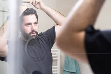 Self haircut. A man is combing his hair before cutting himself - CAVF86002