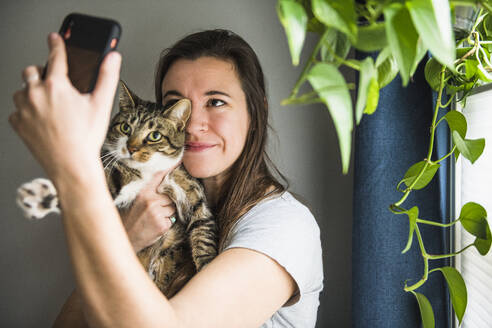Frau zu Hause, die Selfies mit ihrer Katze am Fenster macht - CAVF86018