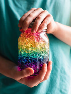 Close up of child's hands holding a jar of rainbow colored crystals. - CAVF86021