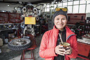 Porträt einer Frau, die in einer Motorradmechanikerwerkstatt Mate-Tee trinkt - CAVF86143