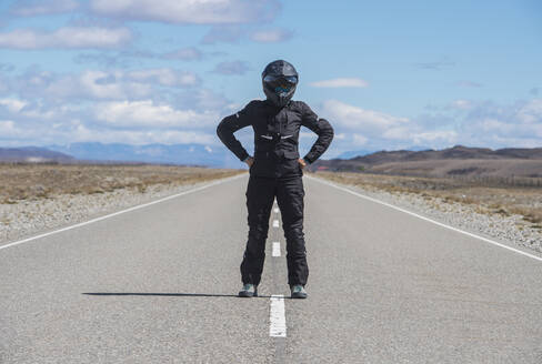 Woman in motorbike gear standing in the middle of empty highway - CAVF86186