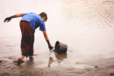 Rear View Of Girl Filling Bucket With Water At Lake - EYF08259