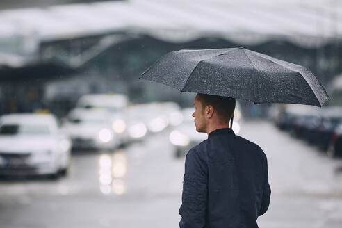 Rückansicht des Mannes mit Regenschirm stehend auf der Straße während des Regens - EYF08267