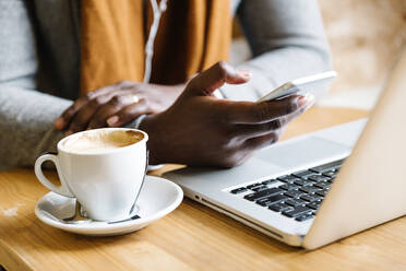 Mittelteil eines Geschäftsmannes, der einen Laptop benutzt, während er Kaffee im Café trinkt - EYF08314