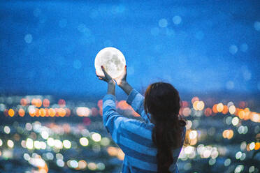 Rückansicht der Frau hält Beleuchtung Ausrüstung in beleuchteten Stadt in der Nacht - EYF08335