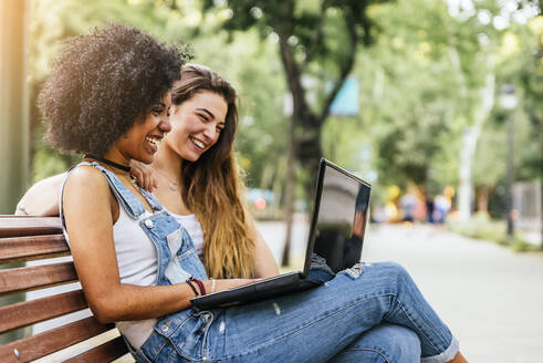 Happy Friends Using Laptop While Sitting On Bench - EYF08338