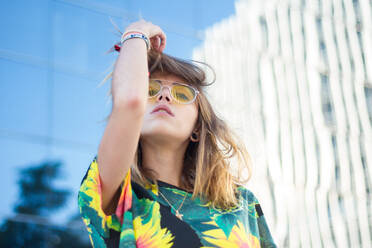 Porträt einer jungen Frau, die eine Sonnenbrille gegen ein Gebäude trägt - EYF08358