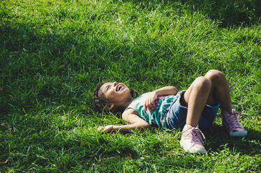 Mädchen lacht, während sie auf einem grasbewachsenen Feld liegt - EYF08377