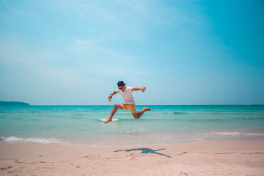 Full Length Of Young Man Jumping At Beach Against Blue Sky - EYF08391