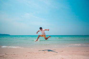 Volle Länge des jungen Mannes Springen am Strand gegen blauen Himmel - EYF08391