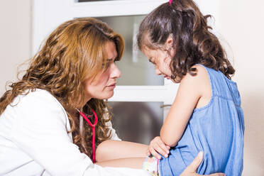 Weiblicher Arzt betrachtet Mädchen, das an Magenschmerzen leidet, im Krankenhaus - EYF08398