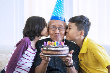Großeltern und Enkelkinder mit Geburtstagskuchen zu Hause - EYF08401