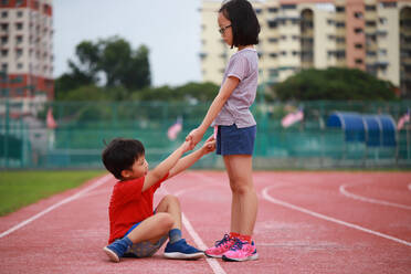 Girl Giving Helping Hand To Friend Fallen On Running Track - EYF08403