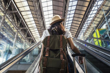 Rückansicht einer Frau, die auf einer Rolltreppe am Flughafen steht - EYF08406