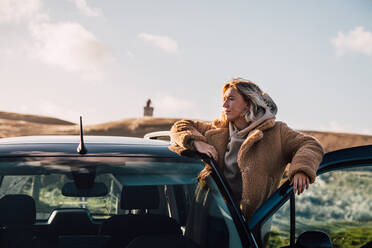 Young Woman Looking Away While Standing By Car Against Sky - EYF08442