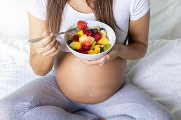 Midsection der schwangeren Frau mit Früchten in der Schüssel zu Hause - EYF08460