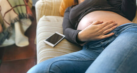 Midsection of Woman Touching Abdomen Während Lying On Sofa zu Hause - EYF08467