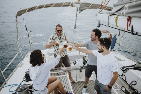 Freunde stoßen mit Bier an, während sie auf einem Segelboot im Meer sitzen - GMLF00287