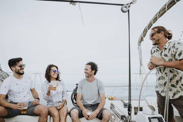 Cheerful friends having fun and enjoying beer on sailboat against clear sky - GMLF00288