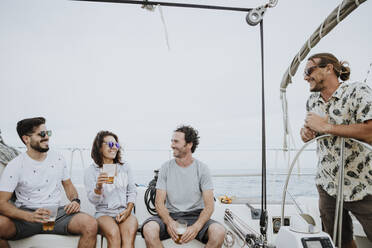 Fröhliche Freunde haben Spaß und genießen Bier auf einem Segelboot gegen den klaren Himmel - GMLF00288